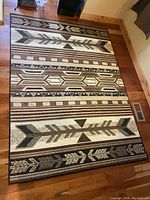 Full view of the indoor area rug with geometric and arrow motifs in multiple earth-tone colors on wooden floor