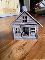 Front view of metal cabin candleholder showing log cabin texture and small windows, closed door.
