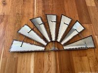 Front view of metal half windmill blade wall hanging on wood floor, showing seven angled blades with weathered finish and rust accents.