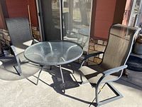 Glass top metal outdoor table with two tan fabric metal frame chairs on a patio, showing overall setup and condition.