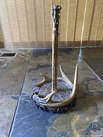 Single resin paper towel holder designed to look like antlers and wood base, placed on stone floor background.