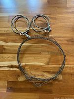 Top view of two gray rope loops and one barbed wire loop laid flat on wooden floor.
