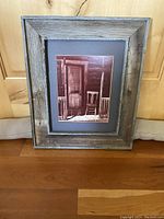 Full front view of the framed sepia tone photograph showing cabin entrance and chair, set in a weathered barn wood frame.