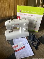 Singer Tradition 2277 white sewing machine next to original box with papers and foot pedal visible