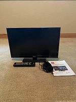 Front view of the RCA flatscreen TV with remote, power cable, and user guide placed in front.