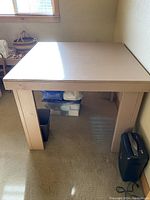 Handmade beige bar height work table shown assembled in room corner with window.