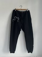 Full view of the black sweatpants showing elastic waistband, drawstring, and elastic ankle cuffs with snake design on upper thigh.