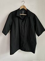 Front view of the black short-sleeve button-up shirt hung on a wooden hanger.