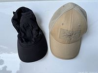 Photo showing the black Lululemon visor cap with extended black fabric and the tan Arcteryx cap side by side.