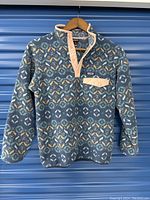 Front view of Patagonia Synchilla patterned fleece sweater with pink snap-button placket and chest pocket flap hanging on wooden hanger.