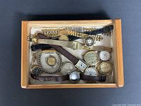 Top-down view of a box containing 12 assorted vintage watches with various bands and dial shapes, mostly women's styles with some men's.