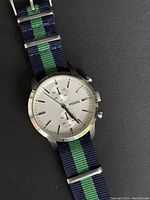 Front close-up of the Fossil chronograph watch face showing silver dial, three subdials, and blue-green striped nylon strap.