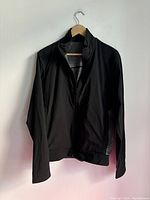 Front view of a black and gray Lululemon men's zip-up jacket hanging on a wooden hanger against a white wall.