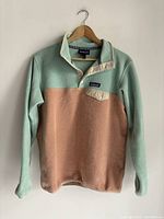 Full view of two-tone Patagonia Synchilla Snap-T fleece top hanging on wooden hanger showing front snaps and chest pocket.