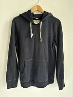 Front view of black Reigning Champ hoodie with white drawstring and kangaroo pocket on hanger.