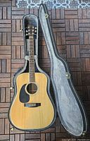 Full view of guitar seated in open hard shell case on patio tile