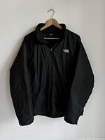 Front view of the black jacket hanging on wooden hanger, showing full length and zipper.