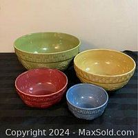 Four nesting stoneware bowls in green, yellow, red, and blue, arranged by size