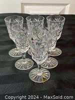 Set of six crystal glasses arranged in two rows on a black cloth, displaying their intricate cut designs and clear glass composition.
