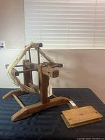 Wooden wool winder with yarn wrapped around and one of the pair of wooden wool carders on a black surface under a window light.