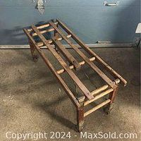Full view of the antique wooden tub bench showing wooden slatted top, frame, and wheels.
