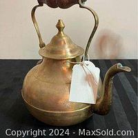 Brass kettle with wooden handle shown from front angle, highlighting the spout and lid.