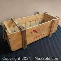 View of the wooden crate showing metal reinforcements, rope handles, and red markings including 'GLASS' and an arrow sign.