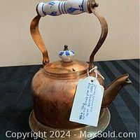 Copper kettle with curved copper handle featuring blue and white ceramic grip and matching ceramic lid knob shown against a neutral background.