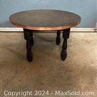 Front angled view of round side table showing hammered copper top and carved wooden legs.