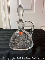 Photo of crystal decanter with stopper, showing full front and side profiles on black cloth background.