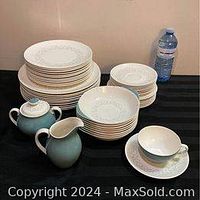 Photo of stack of dinner plates, lunch plates, dessert plates, and bowls along with creamer, sugar bowl with lid, and teacup on black cloth background