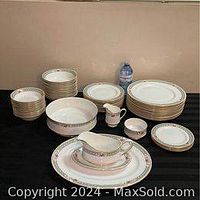 Full set of stacked plates, bowls and serving pieces on black surface with water bottle for scale