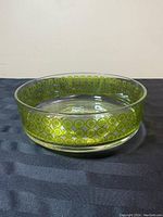Front angle view of the round glass dish showing the green patterned enamel circles around the sides.