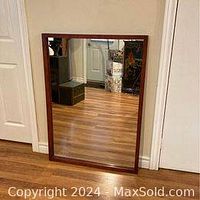 Full view of the rectangular mirror with solid wood frame leaning against the wall, reflecting hardwood floor and surroundings.