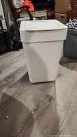 Plastic white rectangular garbage can with hinged lid closed on floor.