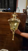 Close-up photo of a brass coach light held by hand showcasing the lantern design and finish.