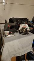 Photo showing Craftsman jig saw, mini circular saw, and carrying case on a grey cloth surface