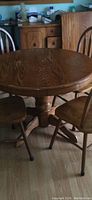 Round solid wood dining table with pedestal base shown with three chairs around it and 18-inch leaf on top.