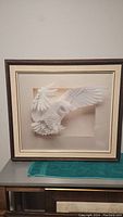 Framed paper artwork of a white owl with wings spread, mounted and matted in a dark wooden frame.