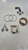Full overview photo showing all jewelry items including earrings, bracelets, and rings on white textured fabric.
