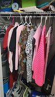 Various women's shirts and tops on hangers including patterned blouse, knitted cardigan, leopard print shirt, and solid color shirts in pink, black, beige, and red.