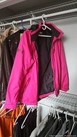 Three jackets hanging on a rack showing pink Helly Hansen and brown leather jacket