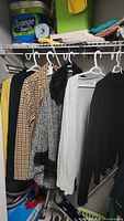 Five ladies sweaters hanging in a closet in colors black, grey, black and white pattern, and brown checkered pattern.