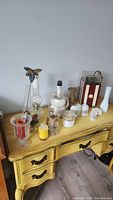 Various oil lamps, candles, and small decorative items on a vintage yellow painted desk.