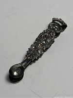 Overall angled side view of the silver sugar tongs showing embossed floral and swan design with monogram on the tong end.