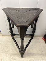 Front perspective view showing triangular carved top with feather leaf patterns and three carved legs connected by stretchers.