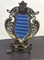 Front full view of the antique cast bronze mirror showing intricate frame and claw feet with a shaped beveled glass mirror inset.