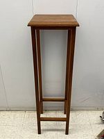 Front view of the tall wooden pedestal table showing square top and leg structure