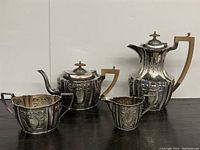 Full view of four-piece antique Sheffield plate silver tea and coffee set showing teapot, coffee pot, sugar bowl, and creamer with ornate embossed designs and wooden handles