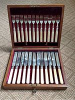 Angled close-up of knives with bone handles and silver collars, showing condition including splits.